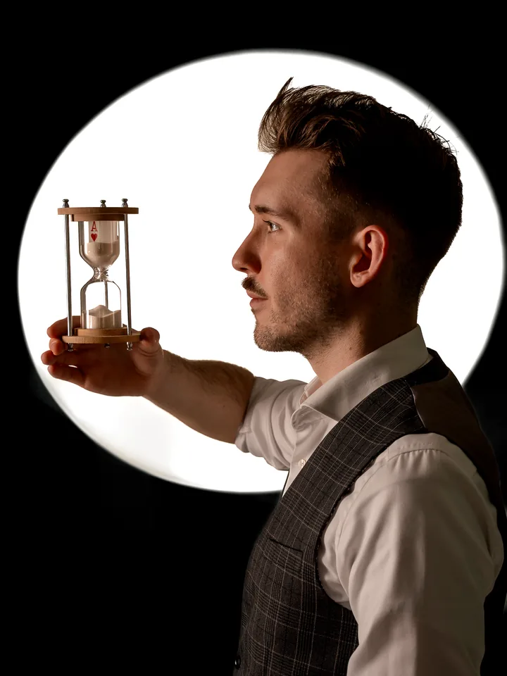 Maxi Muschaweck mit einer Sanduhr, in der eine Spielkarte verrinnt.
